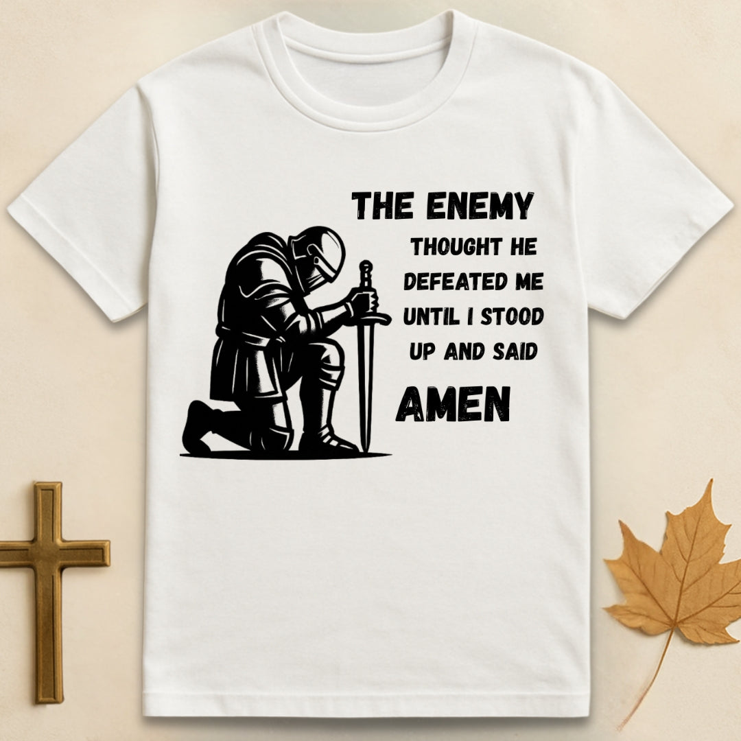 White Amen t-shirt featuring kneeling soldier graphic with sword planted in the ground and text "The enemy thought he defeated me until I stood up and said Amen".